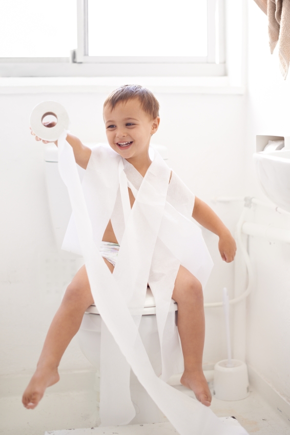 Humorous shot of a young boy sitting on a toilet wrapped in toilet paper