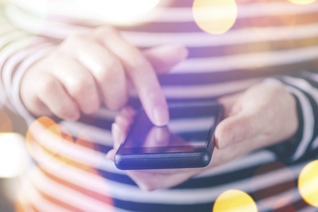 Female hands texting on smartphone, casual woman typing message on touch screen mobile phone device by the window in the morning, nice bokeh, close up with selective focus and shallow depth of field.